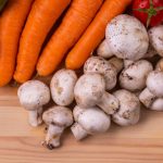 A variety of fresh organic vegetables including carrots, mushrooms, and tomatoes on a wooden table.