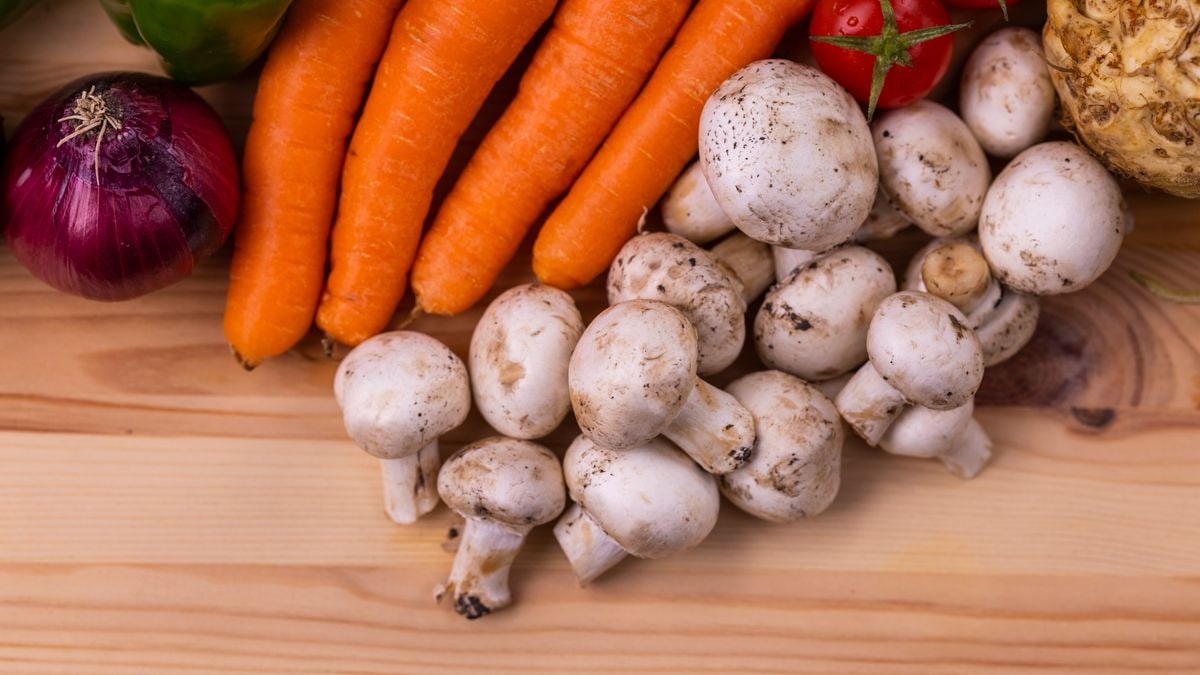 A variety of fresh organic vegetables including carrots, mushrooms, and tomatoes on a wooden table.